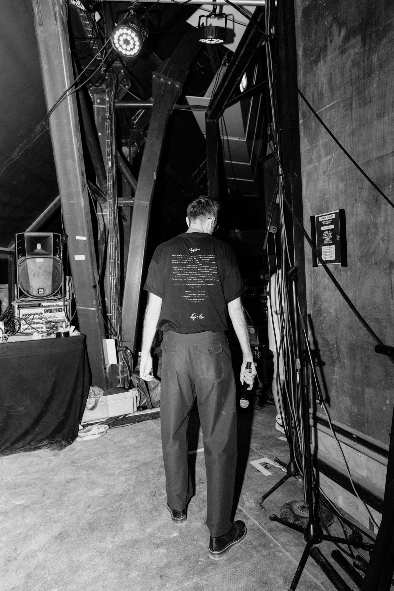 Bedou de dos en coulisses, micro à la main, en noir et blanc